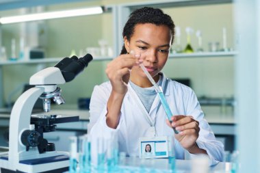 Laboratuvarda yapılan klinik deney sırasında mataradan mavi sıvı madde numunesi alan genç bir kadın farmakolog.