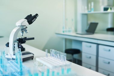 Araştırmacının iş yerinde mavi sıvı maddeler içeren mikroskop ve mataralarla bilimsel veya klinik laboratuvarın içi