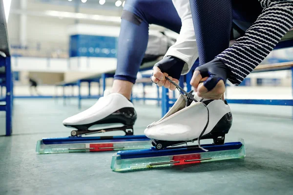 競技前にスケート靴を履いた若いスポーツマンの足や カメラの前のベンチに座ってアイスリンクのトレーニング — ストック写真