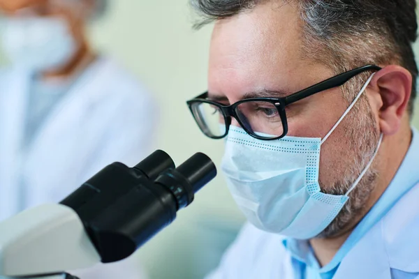 临床实验中戴口罩 戴手套 在显微镜下观察新病毒的经验丰富的药师的密切观察 — 图库照片