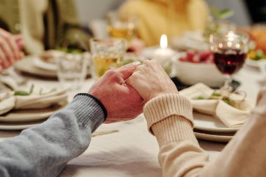 Sevecen yaşlı çiftin elleri Şükran Günü yemeğinden önce ev yapımı yemekler ve yanan mumlarla şenlik masasında dua ediyor.