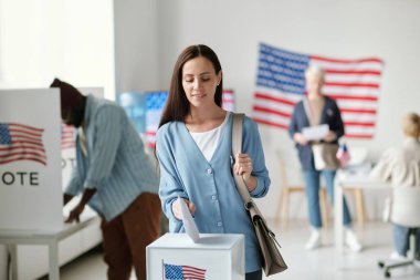 Genç esmer kadın başkanlık seçimlerinde oy verirken oy pusulasını Amerikan bayrağıyla kutuya koyuyor.