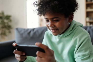 Oturma odasında oturup internetten film izlerken elinde cep telefonu olan kazaklı yakışıklı bir çocuğun yakın çekimi.