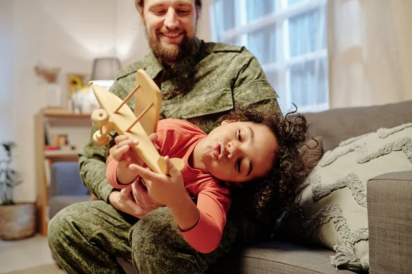 可爱的小男孩手拿木制玩具飞机在父亲的手上玩耍 同时在家里的沙发上玩乐 — 图库照片