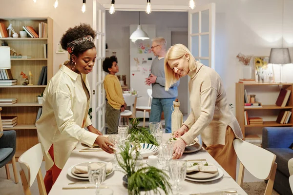 两名身着便衣的跨文化女性 在准备家庭晚餐的时候 为客人端上玻璃杯 盘子和装饰品 — 图库照片