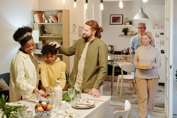 三个不同文化的家庭站在餐桌旁 与从厨房搬到客厅端着自制食品的祖父母相对立 — 图库照片