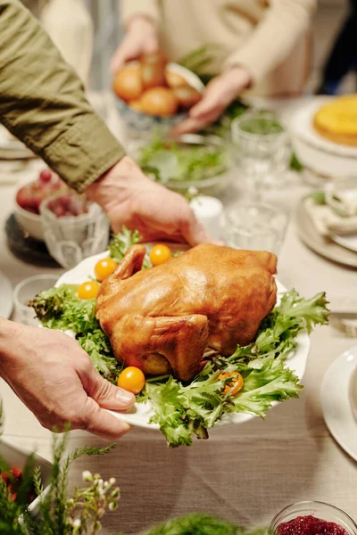 一个拿着烤火鸡和新鲜蔬菜的年轻人 一边端着盘子放在桌上 一边端着自家做的食物当晚餐 — 图库照片