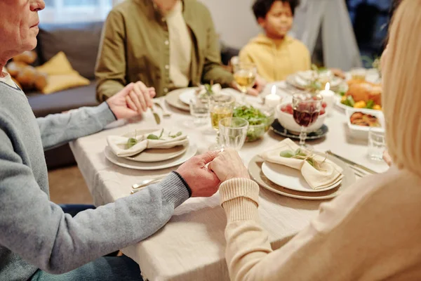 一对年长的夫妇手拉手在节日餐桌旁 在家庭晚宴前祈祷 并配上自制食物和饮品 — 图库照片
