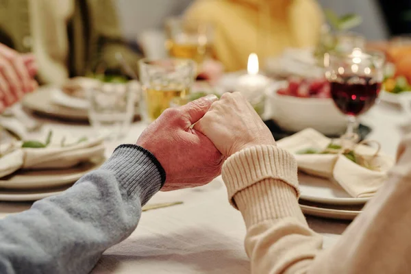 感謝祭の夕食の前に自家製の食べ物や燃えるろうそくとお祝いのテーブルを提供することによって祈って愛情のあるシニアカップルの手 — ストック写真