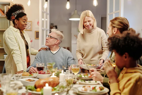 年轻的黑人女人与成熟的男人手挽手 一边站在餐桌旁一边和他说话 一边端上自制的食物 — 图库照片