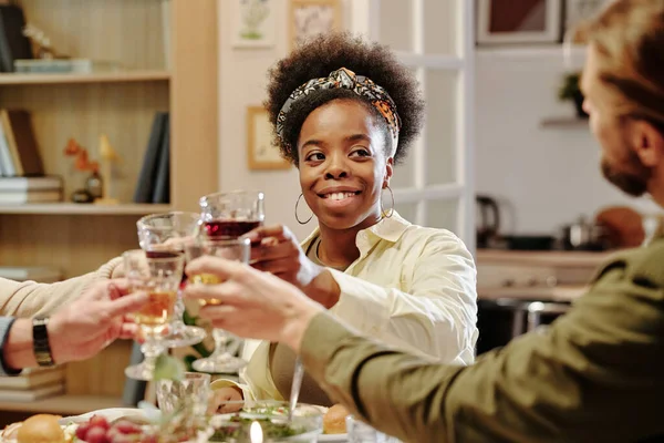 stock image Happy young African American woman looking at her husband while clinking with wineglasses of family members during toast