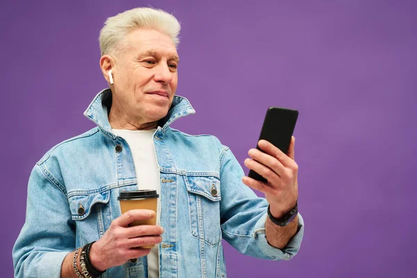 快乐的老年人 带着耳机 一边用智能手机看在线视频 一边用视频聊天 一边喝咖啡 — 图库照片