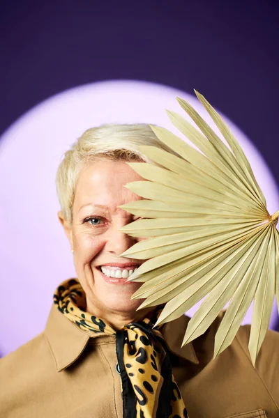 Usmívající Starší Blond Žena Krátkými Vlasy Skrývající Béžový Ventilátor Zatímco — Stock fotografie