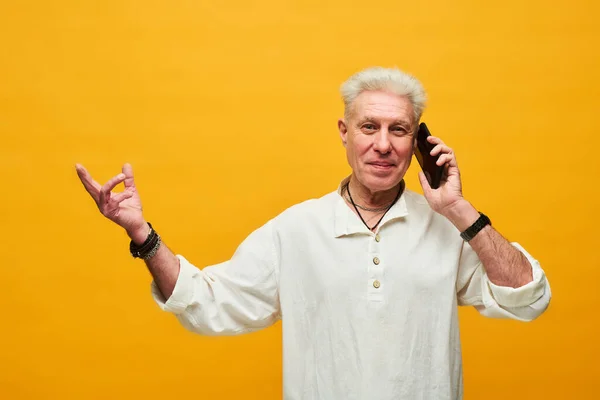 幸せな成熟した男とともに白髪話す携帯電話とカメラを見ながら立ち上がっ黄色の背景で隔離 — ストック写真