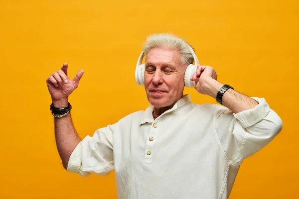 快乐的老人 身穿白衬衫 头戴耳机 站在摄像机前 与黄色背景隔离 欣赏音乐 — 图库照片
