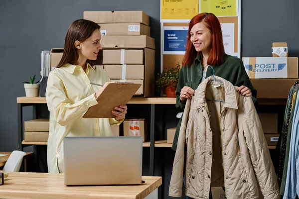 必要としている人々の要求を議論する2人の若い笑顔の女性彼らの1つはドキュメントと同僚にベージュのジャケットを示す — ストック写真