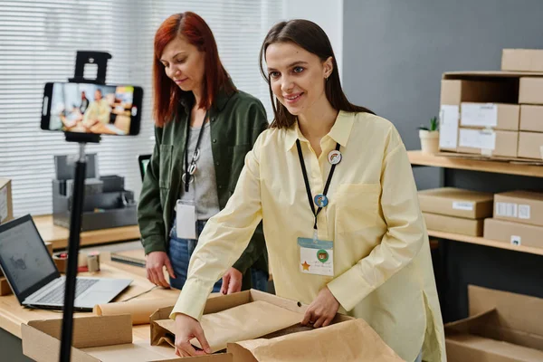 Happy Young Female Volunteer Looking Smartphone Camera While Packing Donation — Stock Photo, Image