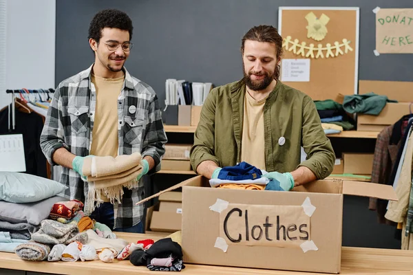 Two Happy Young Intercultural Male Volunteers Preparing Second Hand Clothes — Stock Photo, Image