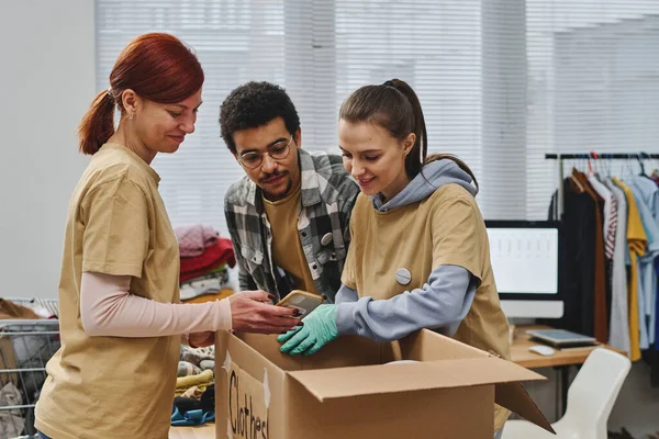 Happy Woman Showing Two Young Intercultural Volunteers Photo Packing Clothes — Stock Photo, Image