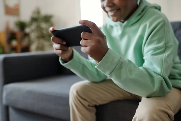 非洲裔美国男孩穿着便服 手持智能手机 坐在客厅沙发上观看网上视频的剪影 — 图库照片