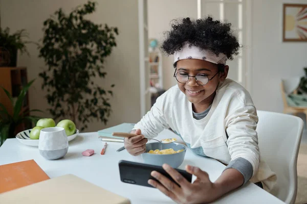 Lächelndes Schulkind Blickt Auf Smartphone Bildschirm Und Isst Müsli Mit — Stockfoto