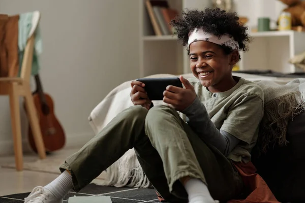 穿着便服的可爱男孩坐在地板上 一边在智能手机屏幕上观看在线视频 一边享受周末的家庭生活 — 图库照片