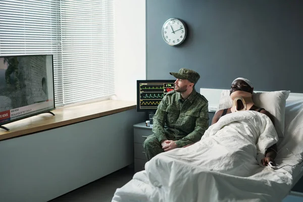 Νεαρός Στρατιώτης Στρατιωτική Στολή Κάθεται Στο Κρεβάτι Του Τραυματισμένου Φίλου — Φωτογραφία Αρχείου