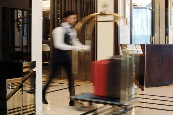 ラウンジや豪華な5つ星ホテルのホールに沿って素早く歩くベルボーイのブラリーモーションや観光客の手荷物でカートを押す — ストック写真