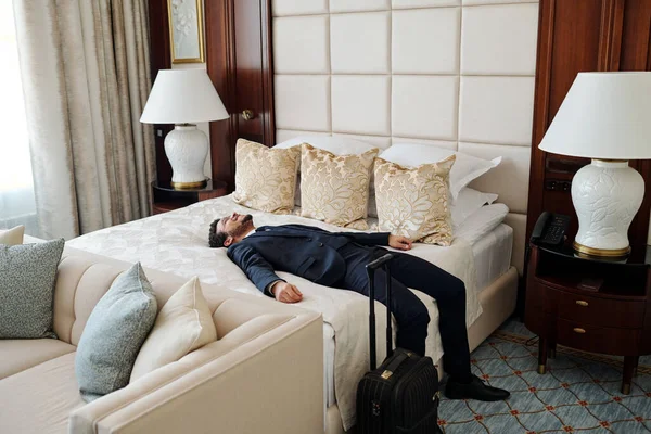 ビジネス旅行中に豪華な5つ星ホテルの部屋で快適なダブルベッドでリラックスしてフォーマルウェアで若い疲れビジネスマン — ストック写真