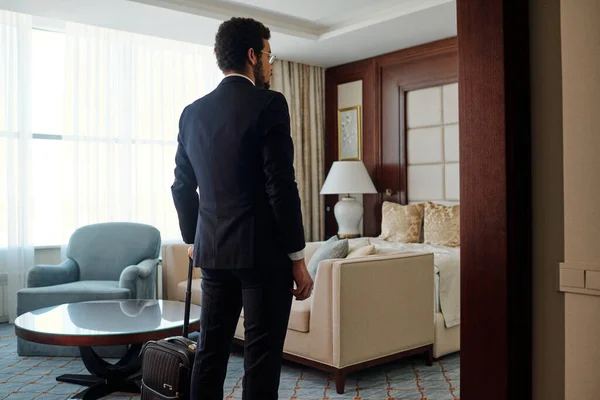 Rear view of white collar worker in elegant suit entering room of luxurious five star hotel on arrival in foreign country during business travel