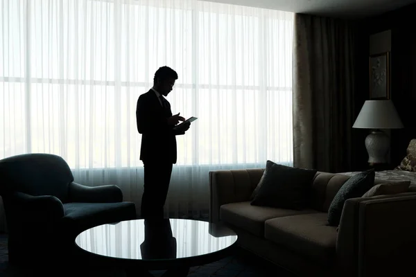 ホテルの部屋に白いシフォンカーテンで覆われた大きな窓に立っている間 タブレットを使用して若いビジネスマンの概要 — ストック写真