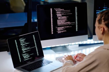 Bilgisayar ekranına şifreli veri ile odaklanırken bilişim mühendisi karanlık ofiste monitörün önünde oturuyor ve bilgiyi deşifre ediyor.