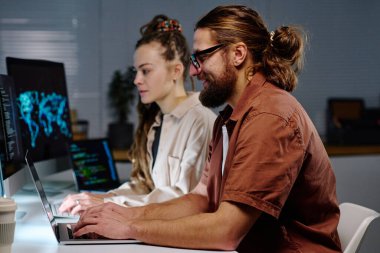 Bilgisayarla kadın iş arkadaşına karşı ekranda veri çözerken dizüstü bilgisayarda daktilo yazan genç erkek bilişim mühendisinin yan görüntüsü