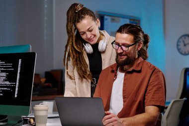 Bilgisayarlı ekrana şifreli verilerle bakan iki mutlu genç programcı ve bunu karanlık ofiste çözmenin yolları hakkında danışmanlık yapıyorlar.