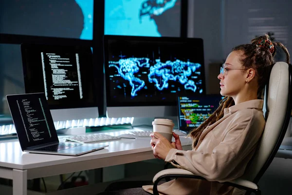 若いです深刻なビジネス女性とともにコーヒーのカップで彼女の職場によってアームチェアに座って コード化されたデータとコンピュータ画面を見て — ストック写真