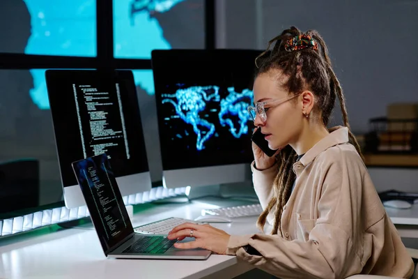 프로그래머 직장에 앉아서 전화로 이야기하고 노트북을 사용하여 밤늦게 자료를 해독한다 — 스톡 사진