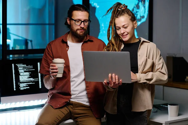 快乐的女性It经理和她的男性同事在笔记本电脑屏幕上浏览在线加密数据 并试图在黑暗的办公室里解码这些数据 — 图库照片