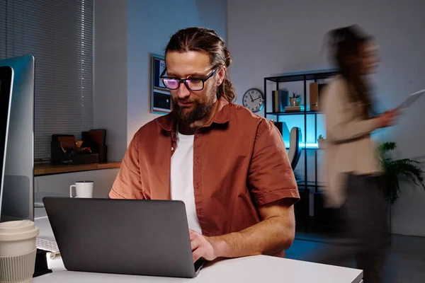 年轻而严肃的男性It工程师坐在笔记本电脑前的工作场所旁边 研究解码软件 防止同事的模糊动作 — 图库照片