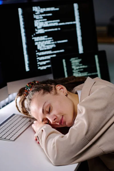 若いです疲れている女性とのスケートで頭を維持しますキーボードによって机の上に暗いオフィスで寝ている間にコンピュータ画面に対してコード化されたデータ — ストック写真