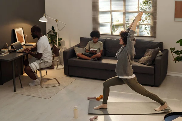 年轻活跃的女性在沙发上和丈夫关系网上用平板电脑在垫子上练习伸展运动对抗儿子的侧视图 — 图库照片
