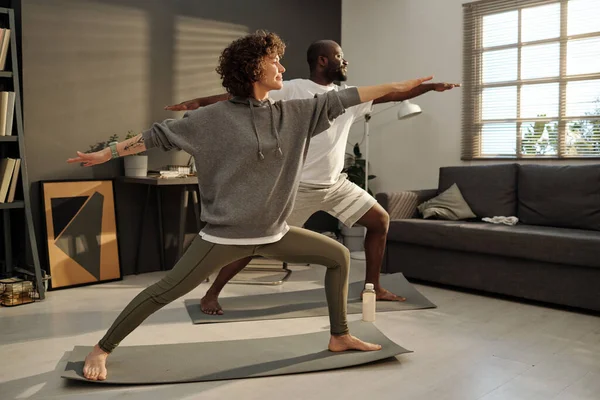 年轻的黑发女子和她的非洲裔美国丈夫站在垫子上 在客厅锻炼时做伸展运动 — 图库照片