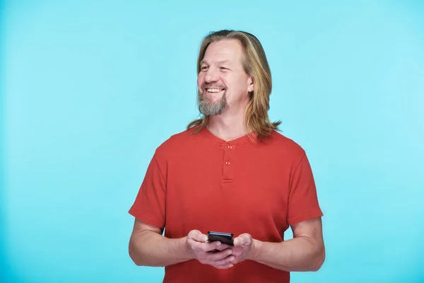 Uśmiechnięty Dojrzały Mężczyzna Korzystający Telefonu Komórkowego Stojącego Niebieskim Tle — Zdjęcie stockowe