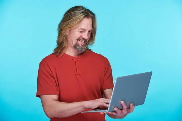 笑顔成熟した男とともに長いです髪タイプのラップトップコンピュータ上に立って青の背景 — ストック写真