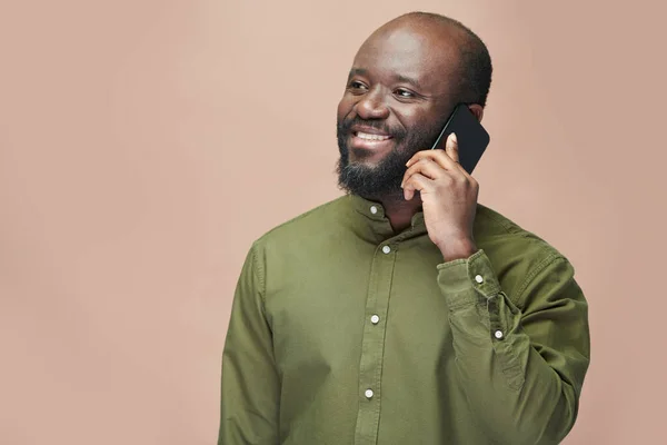 Uśmiechnięty Afroamerykanin Zielonej Koszuli Rozmawiający Przez Telefon Komórkowy Odizolowany Brązowym — Zdjęcie stockowe