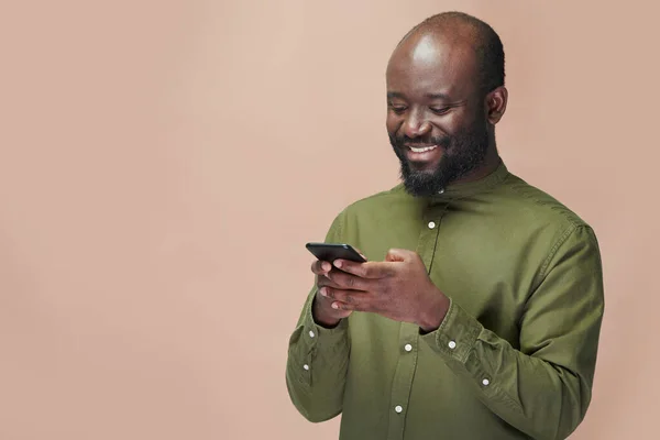 Afroamerykanin Ogląda Wideo Smartfonie Uśmiecha Się Stojąc Brązowym Tle — Zdjęcie stockowe