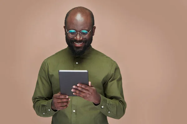 戴眼镜的非裔美国人在数字平板电脑上观看视频 笑着站在褐色背景上 — 图库照片
