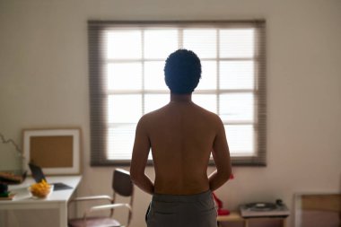 Depresyondaki genç bir adamın dikiz aynasından odada oturup pencereye bakması.