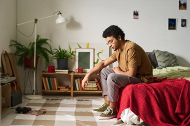 Genç çocuk yatak odasında otururken sorunlarını üzgün bir ifadeyle düşünüyor.