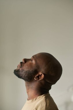 Gri arka planda gözleri kapalı meditasyon yapan Afrikalı Amerikalı bir adamın dikey görüntüsü.