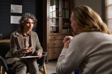 Kendine güvenen psikoterapist, kalıcı stres, kronik veya mevsimsel depresyon yaşayan olgun erkek hastaya bir şey anlatıyor.